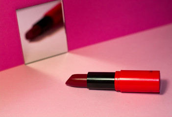 On bright pink background, small square mirror and red lipstick.