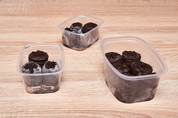 Group of three plastic boxes filled with black soil prepared for planting seeds of plants of seedlings of flowers and vegetables on a wooden table in the house in spring.