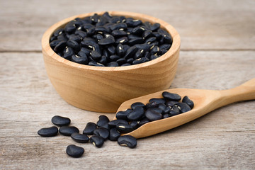 Black bean in wooden bowl isolated on wood table background.