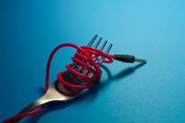 On bright blue background lies fork with wound red cord from headphones as spaghetti. Mobile...