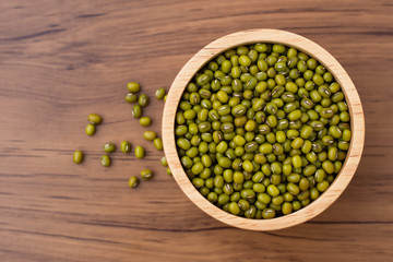 Green mung beans in wooden bowl isolated on wood table background. Top view. Flat lay.
