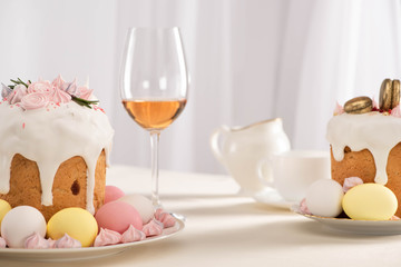 Fototapeta na wymiar delicious Easter cakes decorated with meringue near colorful eggs on plates and wine glass