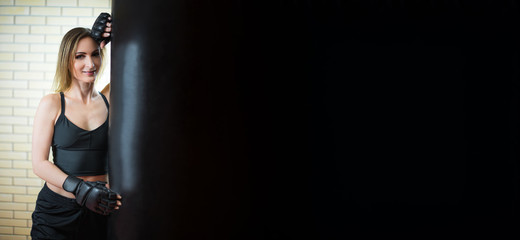 Banner. Beautiful girl and boxing. Girl in sportswear: in a black top and black sports shorts with Boxing gloves , extended mix mma open fingers gloves next to a black punching bag, place for text