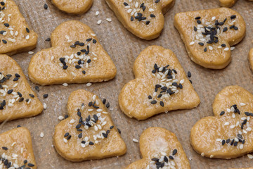 Gingerbread cookie hearts with black and white sesame and sugar on baking paper. The scene of making sweet homemade pastries. Rustic style recipe