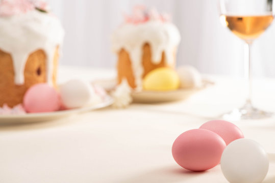 selective focus of delicious Easter cakes with meringue and colorful eggs on plates near wine glass