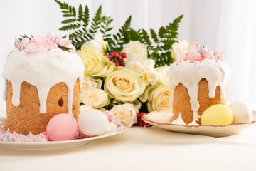 delicious Easter cakes decorated with meringue with colorful eggs on plate near flowers