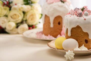 selective focus of delicious Easter cakes decorated with meringue near eggs on plate and flowers