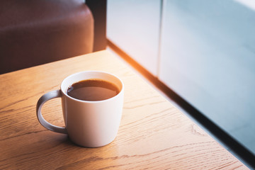 A cup of hot coffee on a wood table background with the light from window