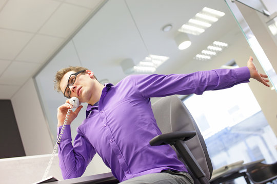 sitting caucasian man office worker with phone in hand, stretching arm and neck , exercising during work  in his office