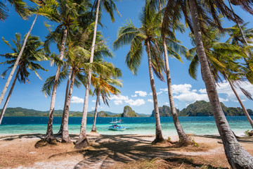 El Nido, Palawan, Philippines. Palm trees on sandy beach. tourist filippino banca boat in turquoise ocean lagoon. Island hopping tour with beautiful tropical scenery