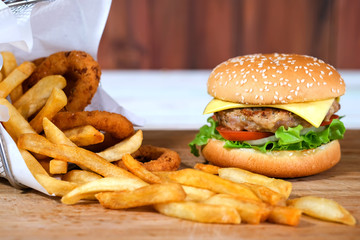 Close-up macro of delicious fresh homemade hamburger with cheese, pork, tomato, onion and vegetable on a wooden plate with french fries basket and onion ring.