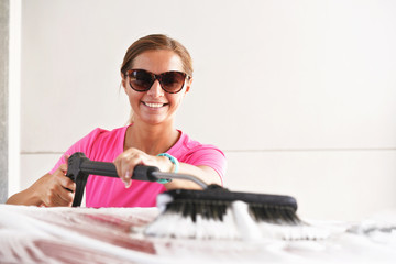 Young woman wearing pink t shirt and sunglasses cleaning her car in self serve carwash, banner with...