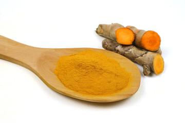 Turmeric powder in a wooden spoon and fresh turmeric roots isolated on a white background is an ingredient in turmeric foods and ingredients in skin care products. Turmeric helps strengthen the skin.
