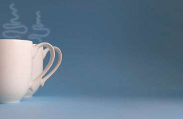 Two cups over which steam rises. The concept of an invitation to a joint tea party and a coffee break. Deep blue background. Close up. Copy space. 