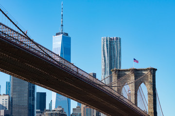 Naklejka premium The Brooklyn Bridge with an American Flag over the East River with the Lower Manhattan New York City Skyline