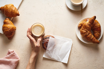 Flatlay with coffee and croissants. Female hand holding a cup of capuccino. Breakfast beverage with pastry. Morning set