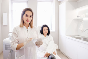 Fototapeta premium Pretty young woman doctor consults her client brunette girl and advertises a new effective drug. Doctor writes a prescription for a contraceptive. Concept of expensive treatment