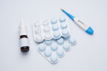 Nasal spray, tablets and thermometer on blue background