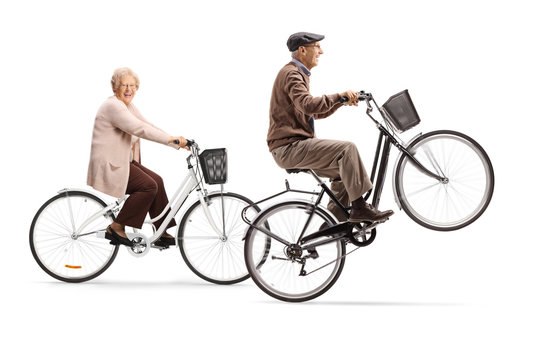 Elderly man lifting a bicycle up on one wheel and senior woman riding a bicycle
