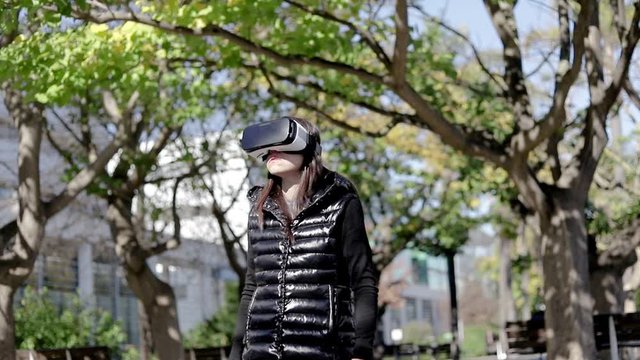 Focused woman in VR headset in park. Handheld shot of concentrated young woman using virtual reality headset outdoors, low angle view. Wearable technology concept