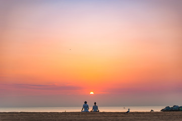 couple doing a relaxing yoga and meditation session on the beach at sunrise with birds and the sun rising