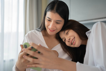 Young  happy asian couple lesbian lover sitting on the bed together and watching cinema from smartphone in bedroom.