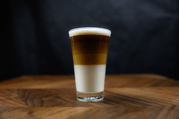 cappuccino freshly brewed into a glass cup showing beautiful layers wooden table