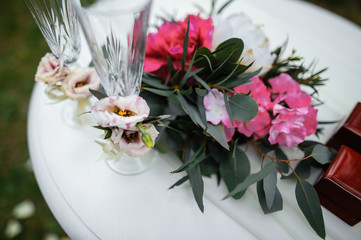 Beautifully decorated wedding glasses for the bride and the groom are on the table. There are flowers and greenery on the table