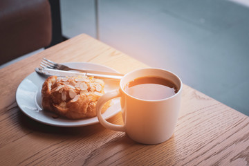 a black coffee cup with Croissant closed up the window with spoon and knife and have light from outside