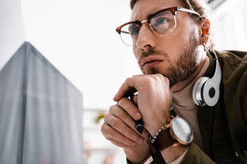 Pensive 3d artist in headphones holding stylus of graphics tablet near computer monitor with black...