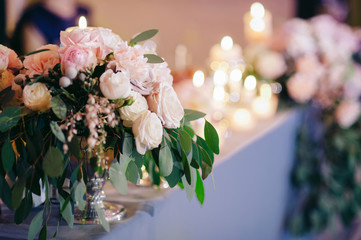 Wedding. Banquet. At the banquet table with a blue tablecloth there is floral composition of pink flowers and greenery, and candles in glass vases