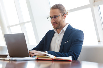 Positive pleased young businessman using laptop computer.
