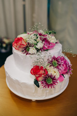 Obraz na płótnie Canvas White wedding cake decorated with red and pink flowers and greenery standing on a wooden table