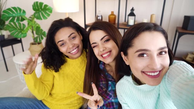 Cheerful girl taking selfie photo with multiracial roommates at home