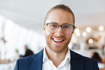 Pleased young businessman indoors in office looking aside.