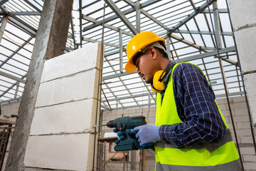 Construction worker use a drill bit,Engineer wearing safety equipment (helmet and jacket) uses a power drill to mount a aerated brick wall.