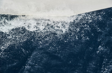 The nose of a sailing white boat cuts water, splashes spray, water glistens on the sunlight
