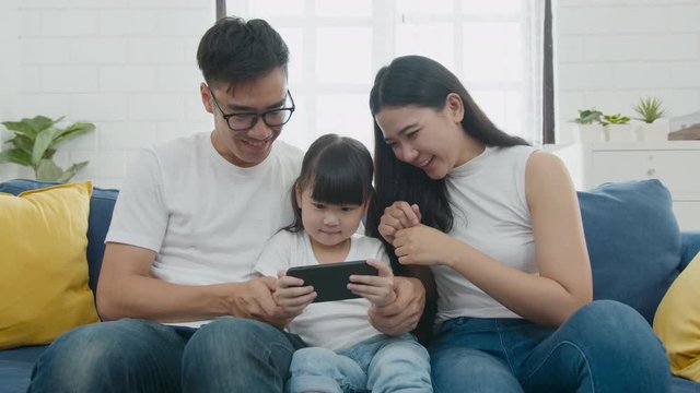 Slow motion zooming shot : Happy warm family father, mother and daughter playing funny game online on smartphone mobile sitting on couch together, parents with kids enjoying mobile apps on smart phone