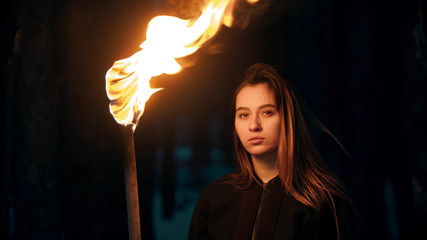 Young beautiful woman with torch in night forest looking in the camera - obrazy, fototapety, plakaty