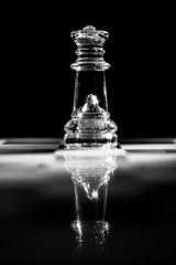 Obraz na płótnie Canvas Single clear glass queen chess piece or figure standing on glass chessboard with reflection. Isolated on black background with copy space. Black and white photography.