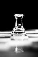Single clear glass rook chess piece or figure standing on glass chessboard with reflection. Isolated on black background with copy space. Black and white photography.