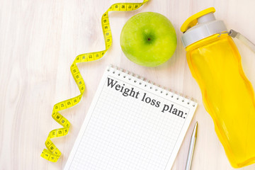 green apple, measuring tape and notebook for writing with the inscription weight loss plan on a...