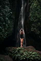 A woman does yoga at a waterfall. Healthy lifestyle. The concentration of the body. A woman does yoga in Bali. A woman meditates in nature. Meditation at the waterfall. Young woman practicing yoga