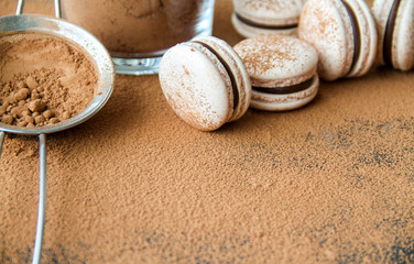 French dessert macaron powered with cocoa powder and filled with dark chocolate ganache. Macarons are on a dark background sprinkled with cocoa powder. 