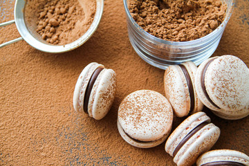 French dessert macaron powered with cocoa powder and filled with dark chocolate ganache. Macarons are on a dark background sprinkled with cocoa powder. 