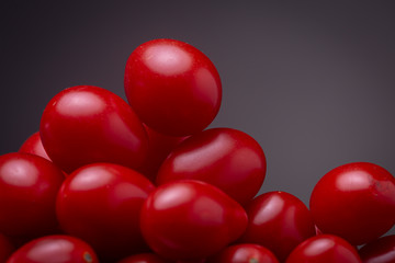 Super close up of a stack of vibrant red cherry tomatoes against a dark grey background