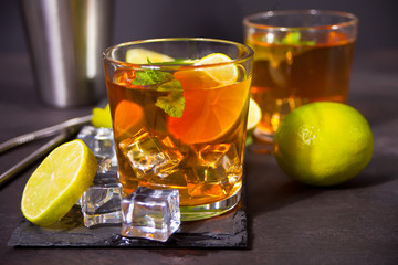 Fresh cocktail Cuba Libre with brown rum, cola, mint and lime on black background. Long Island Iced Tea cocktail.