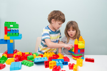 Little kids playing with lots of colorful plastic blocks constructor and builds the robot indoor. 