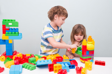Little kids playing with lots of colorful plastic blocks constructor and builds the robot indoor. 