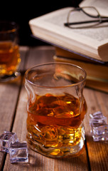 whiskey with ice on a wooden table. Nearby old books.
